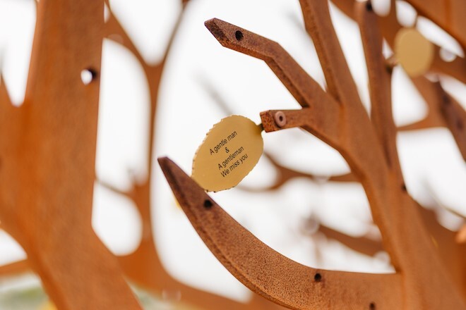 "Image depicts a memorial of a metal bronze coloured tree decorated with leaves engraved with messages"