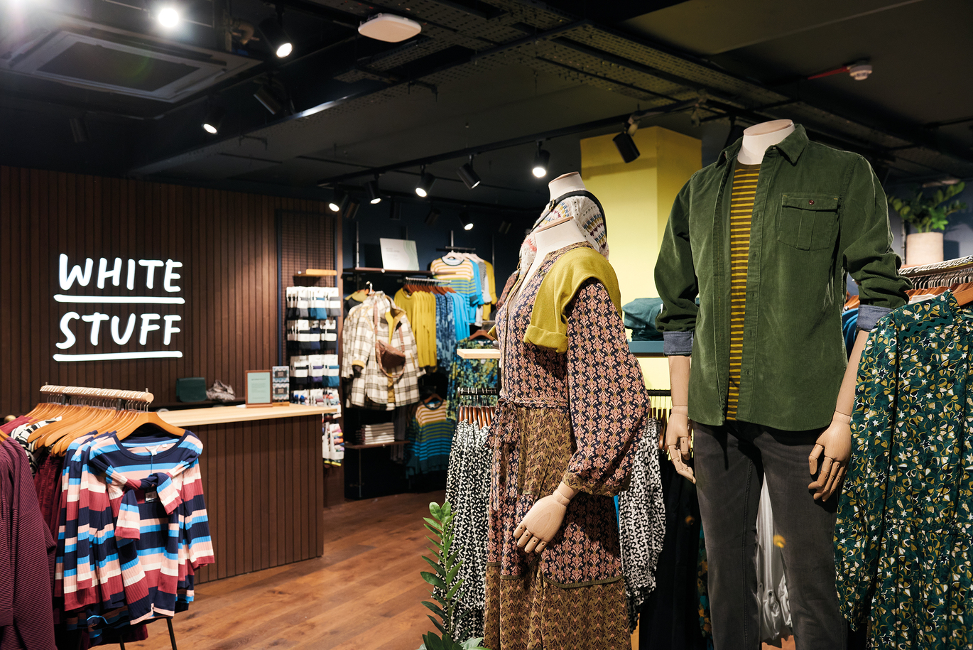 View inside a store with clothes hanging and mannequins with the till behind.