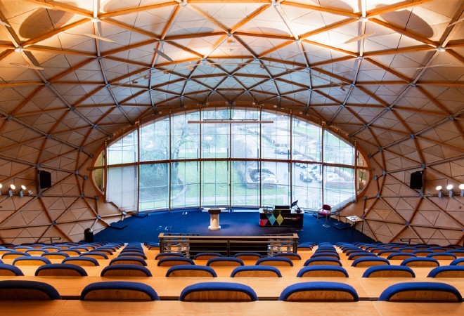 "Lecture theatre with graduated seating and rounded white panel and wooden bar ceiling"