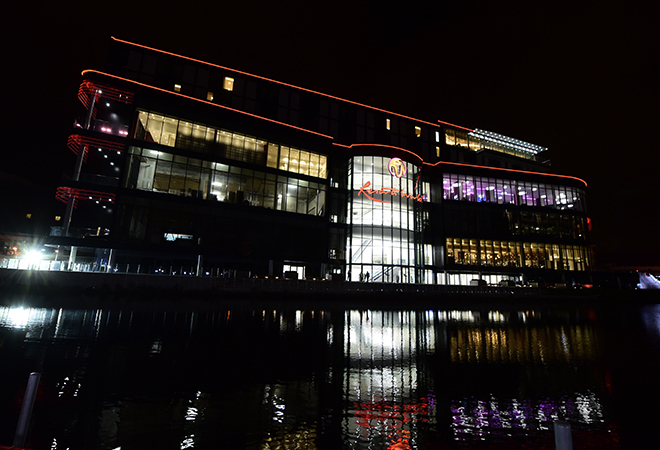"A photo of Resorts World Birmingham Shopping Centre at night. The river as at the front of the photo, the entrance to the centre is lit up inside the building."
