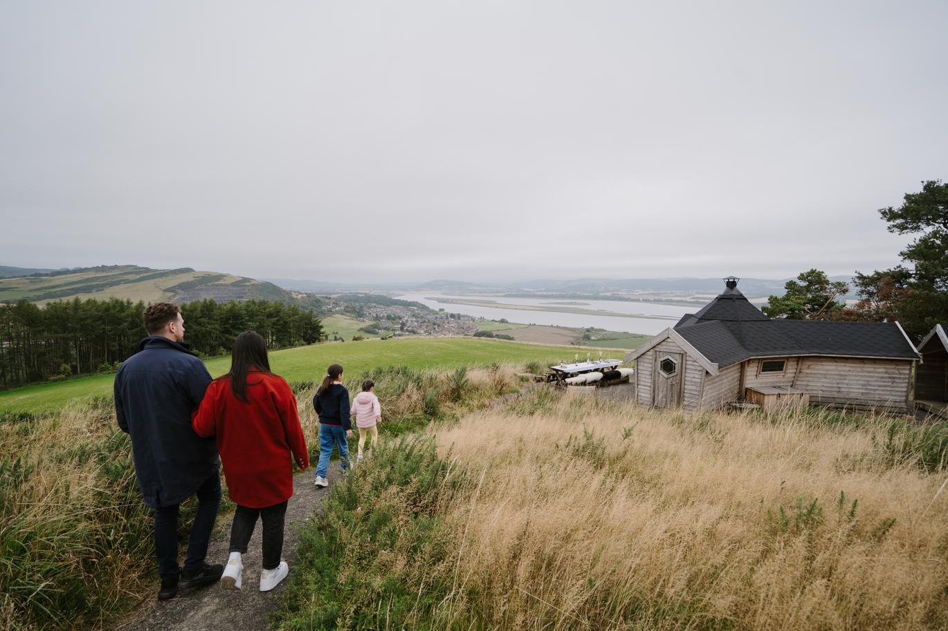  "A man, a woman and two girls walking towards The Hide at Lindores Stay, Fife, Scotland."