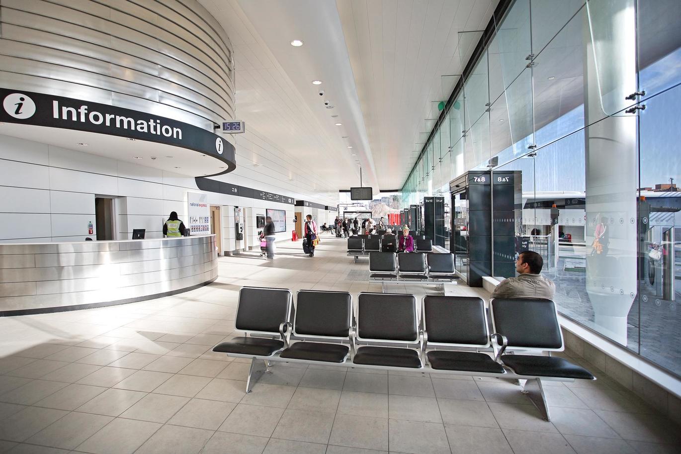 "A photos of inside a National Express coach station with seating available to the right, a clear floor to ceiling window on the right and an Information Desk to the left."