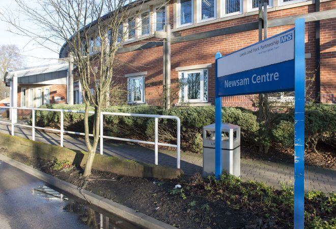 The front of the building with the blue and white sign that reads 'Newsam Centre' with a stepless slope with white railings leading up to the entrance.