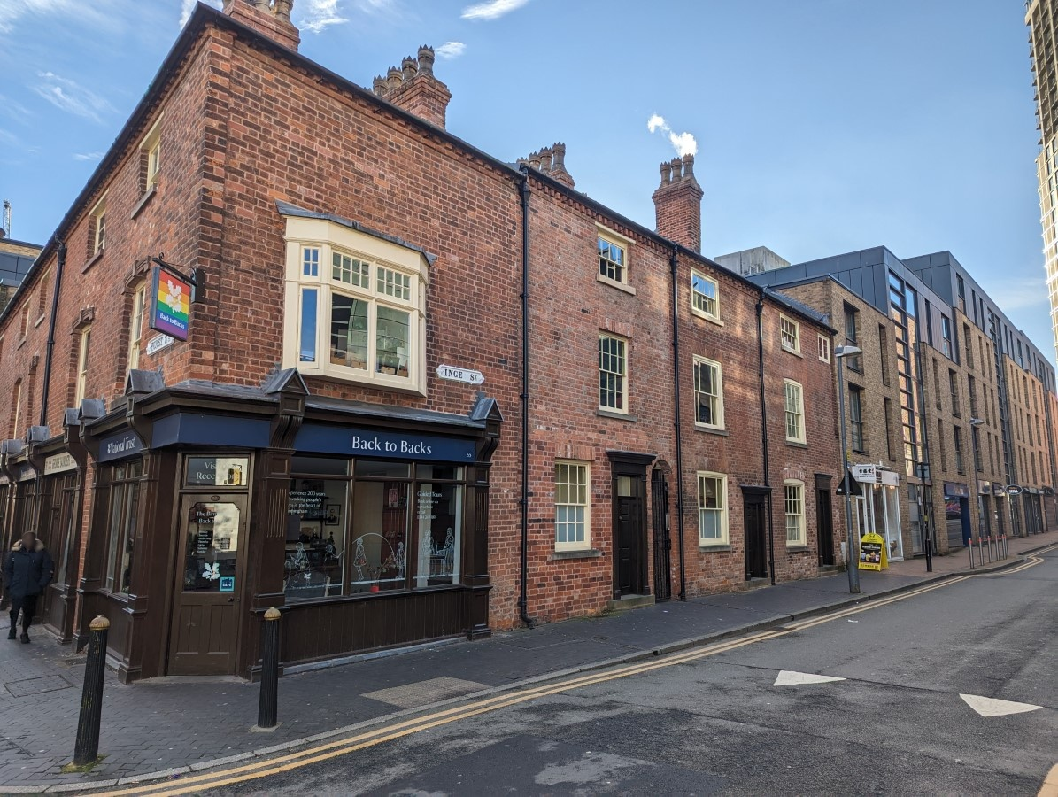A street corner with a brick building on the corner and going off in either direction along the street. 