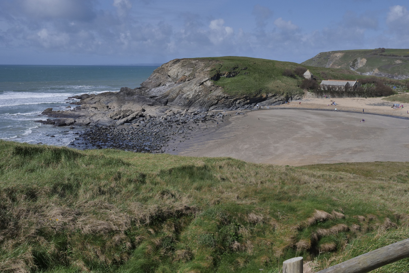 View from the top of a hill of the beach at Church Cove with the grassy cliffs behind.