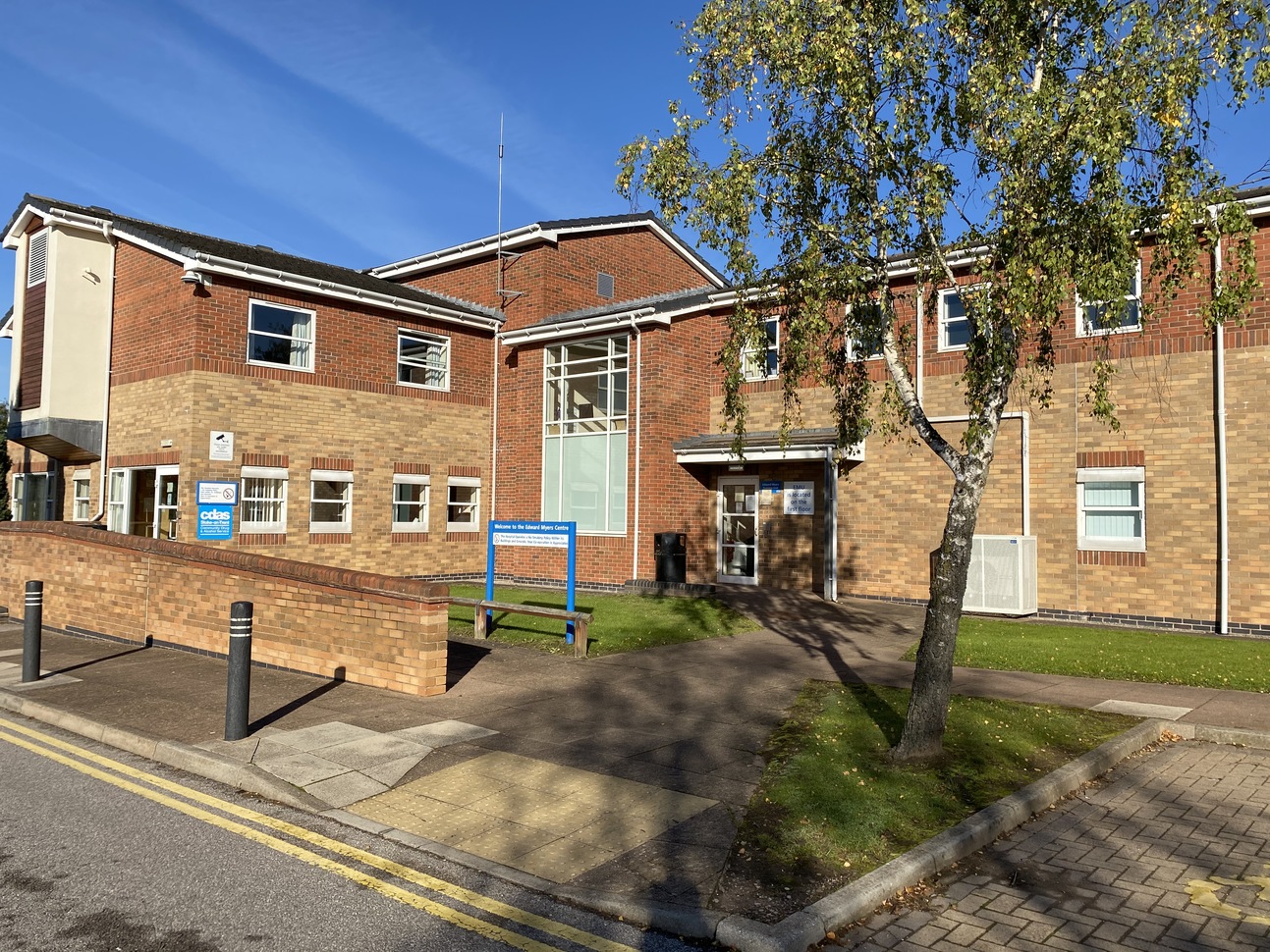 Accessible entrance to the EMU building. There is a small tree and signs showing what departments reside in the building.