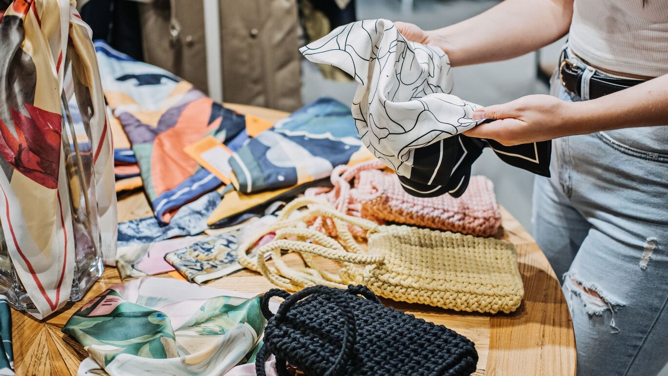 "Image of internal shop display with the bottom half of a person browsing the clothing, having picked up a black and white piece of fabric"