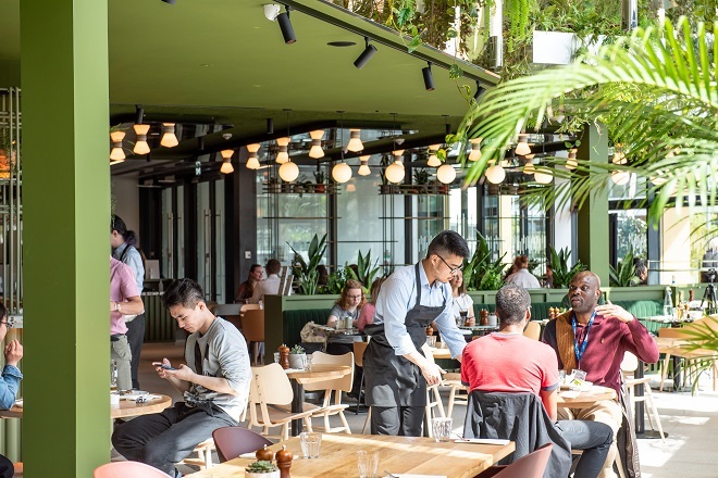 "Photo of restaurant with people seated at tables being served."