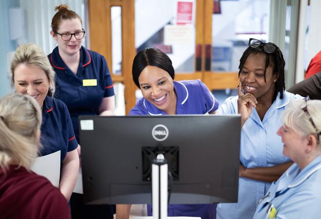 "Nurses gathered around a computer screen"