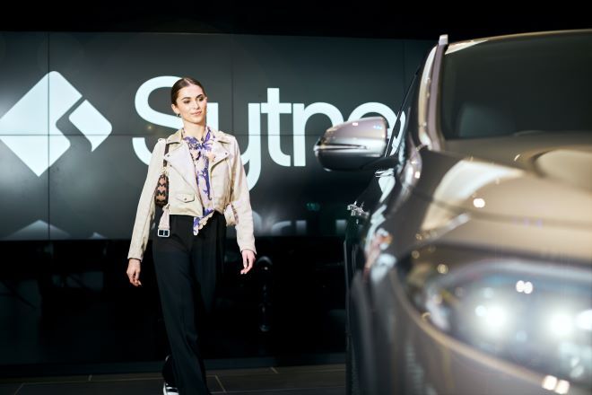 "A colleague walks next to a new car, with a large sign that says Sytner in the background"
