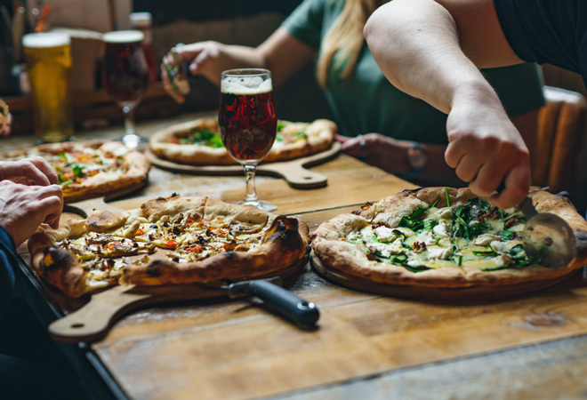 "Photo of a table in a Brewdog Bar, four people served with a pizza each. One person is cutting their pizza"