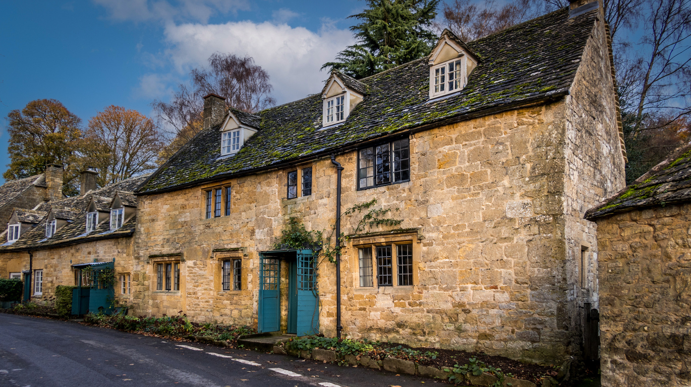 The exterior of the stone built Snowshill Manor Farmhouse right on the road with trees behind.