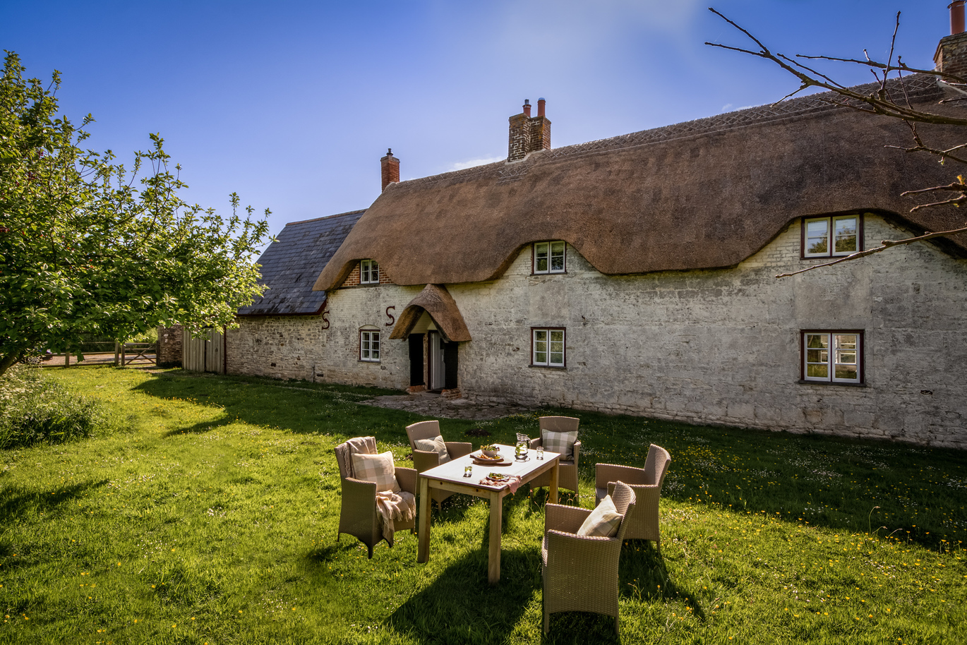 The outdoor seating area in the garden at Middlebere Farmhouse, with the thatched building behind.