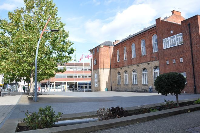 "photo of worksop old market square. a large tree is on the left, and a two storey brick building stands on the right. a large square is open in the middle."