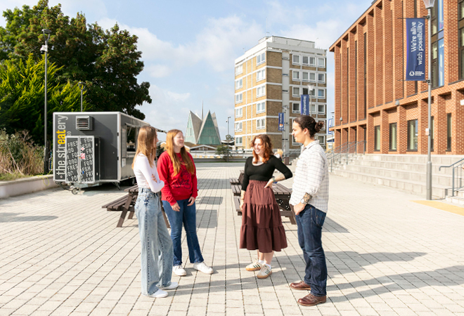 "Image of four students chatting to each other outside whilst stood on the Canterbury campus"
