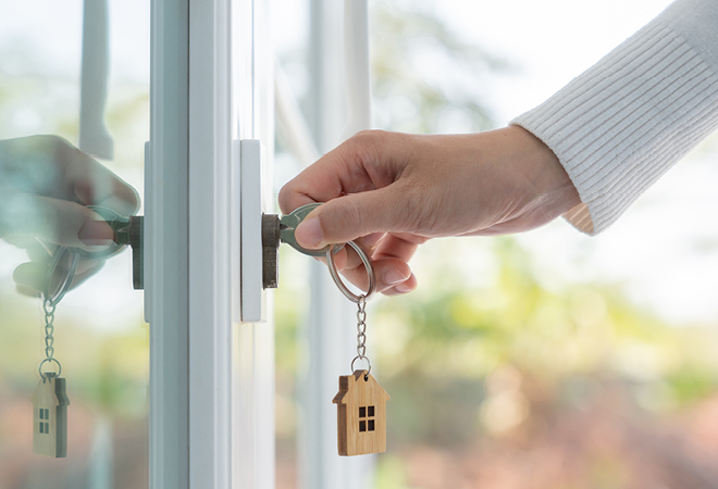" a person is turning a key in a glass door. a wooden keyring is hanging with the countrywide logo on it"