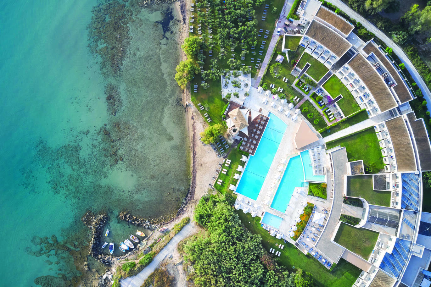 Birdseye view of the hotel complex right on the beach with some small boats in the blue sea.