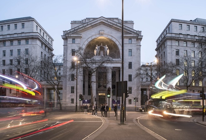 "Exterior image of 3 white University buildings with a street in the forefront"