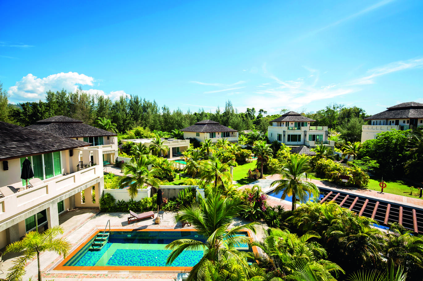 View of part of the hotel complex and pool area surrounded by lots of green lawns and palm trees with the blue but slightly cloudy sky above.