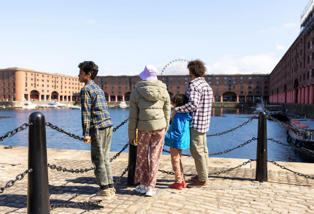 4 people stand with thier backs to the camera looking out at the liverpool docks 