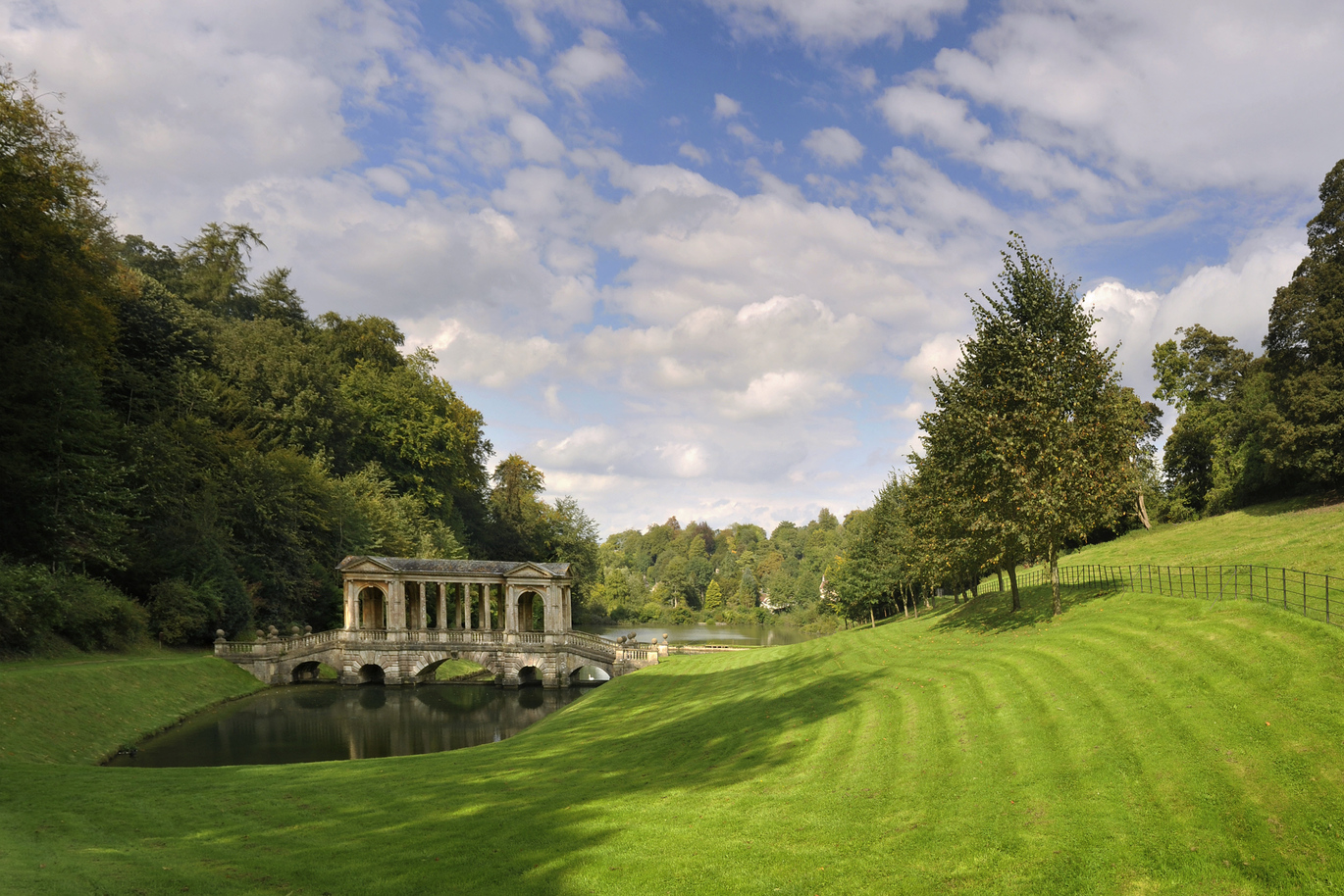 The 18th century Palladian Bridge over the river at Prior Park Landscape Garden surrounded by lush green grass and many many trees.