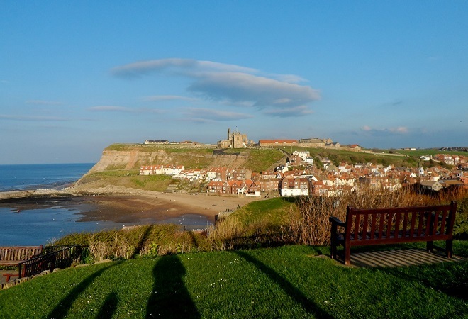 on top of a hill overlooking the beach, coastline and a similar sized hill in the background. There is a castle on the hill in the background also.