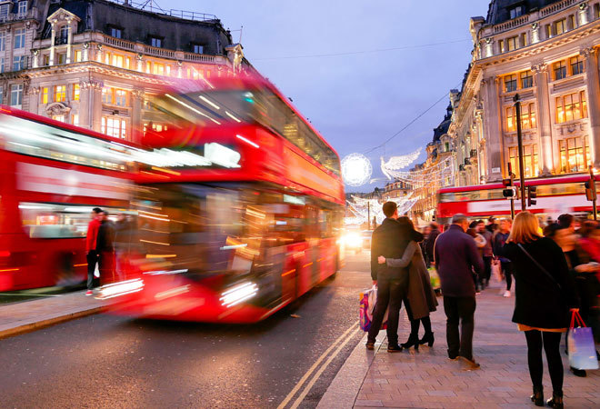 photo of a busy london street. Lots of pedestrians walk past, and two embrace. A double decker bus is blurred as it drives past.