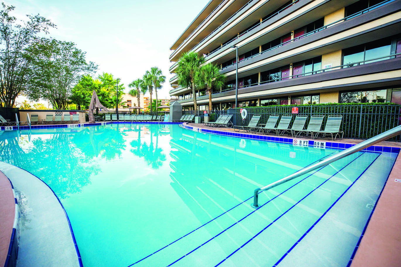 View from the pool area with the tall hotel building to the side and a few deck chairs around the pool.