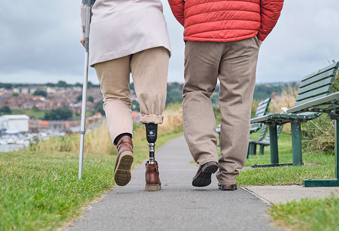 "Couple on a hike, using a walking stick and with a prosthetic limb"