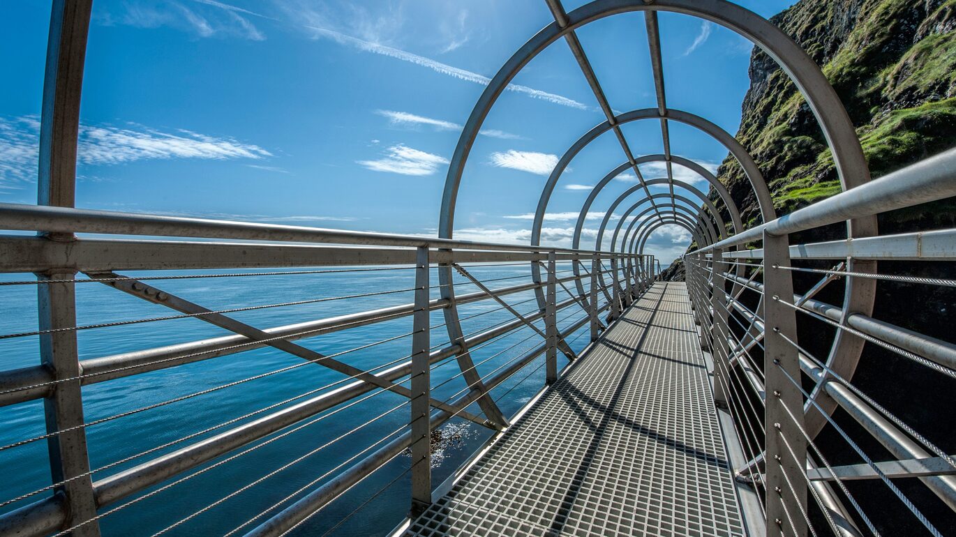 "Gobbins Centre metal bridge scaling the side of the rocks overlooking the blue sea"