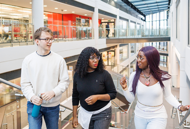 "Image of three students chatting whilst walking up the stairs in a building at Canterbury campus"