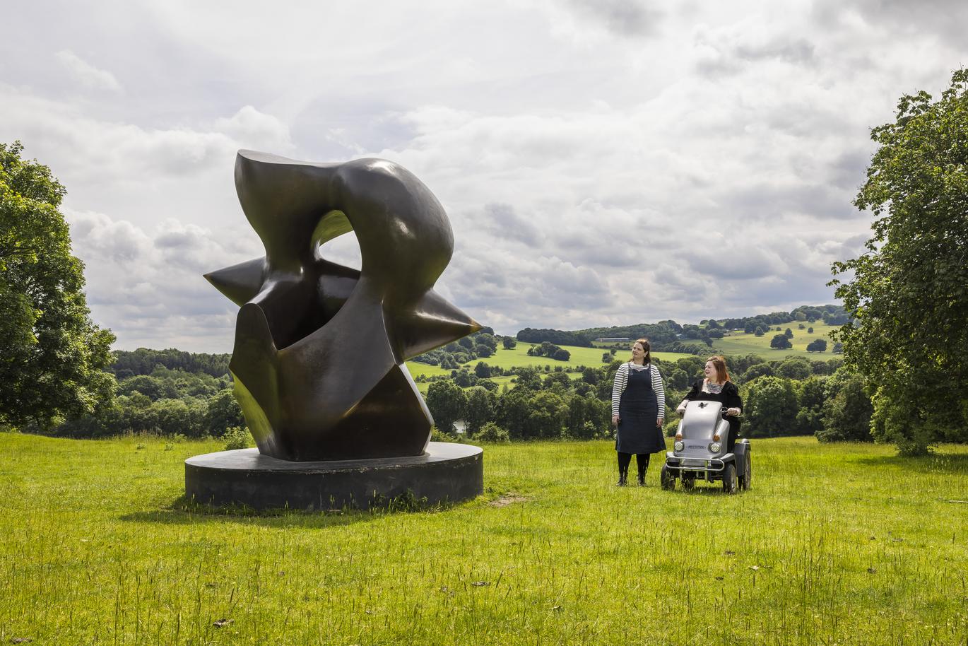 "Two women look at a Henry Moore sculpture at The Yorkshire Sculpture Park, Wakefield. One of the women uses a disability scooter."