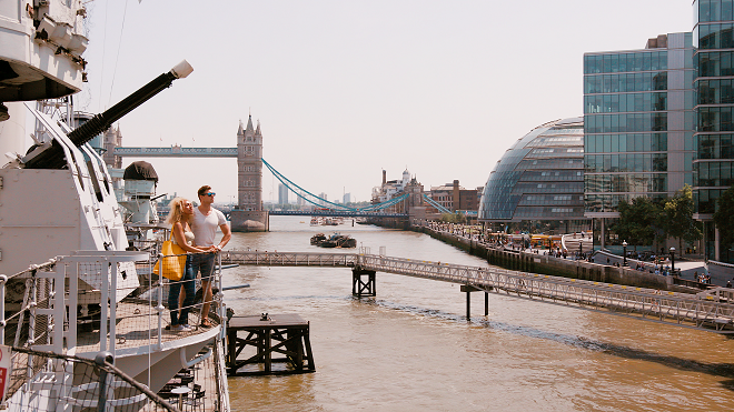 2 people on the viewing platform from HMS Belfast looking out at London across the river with Tower Bridge in the background