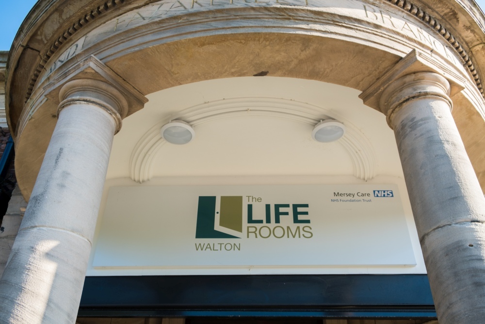 "A close up image of a sign on the entrance to a building which reads 'The Life Rooms Walton'. The entrance to the building has two large stone pillars."