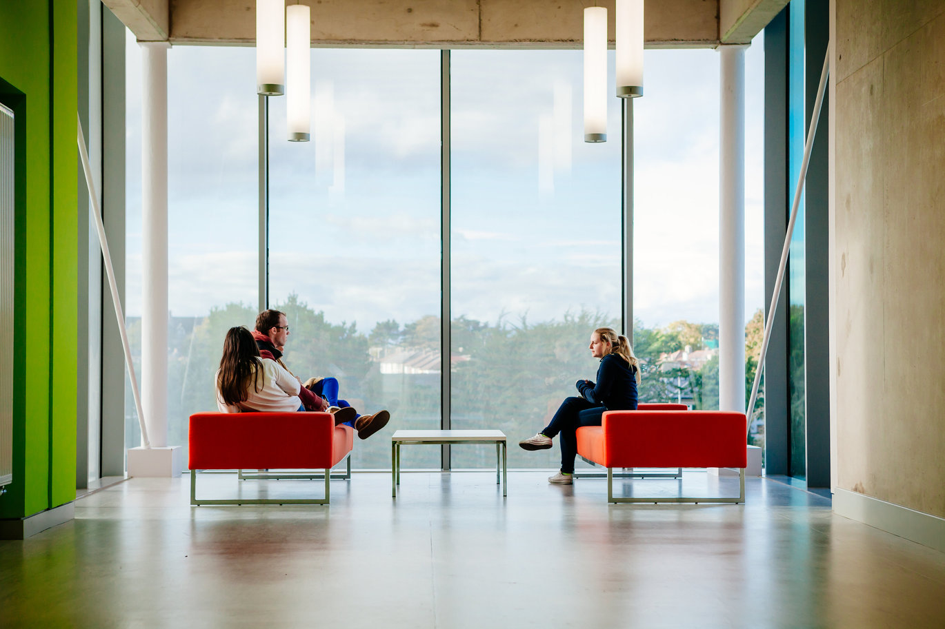 "Two students sitting on couches facing each other in front of a large window"