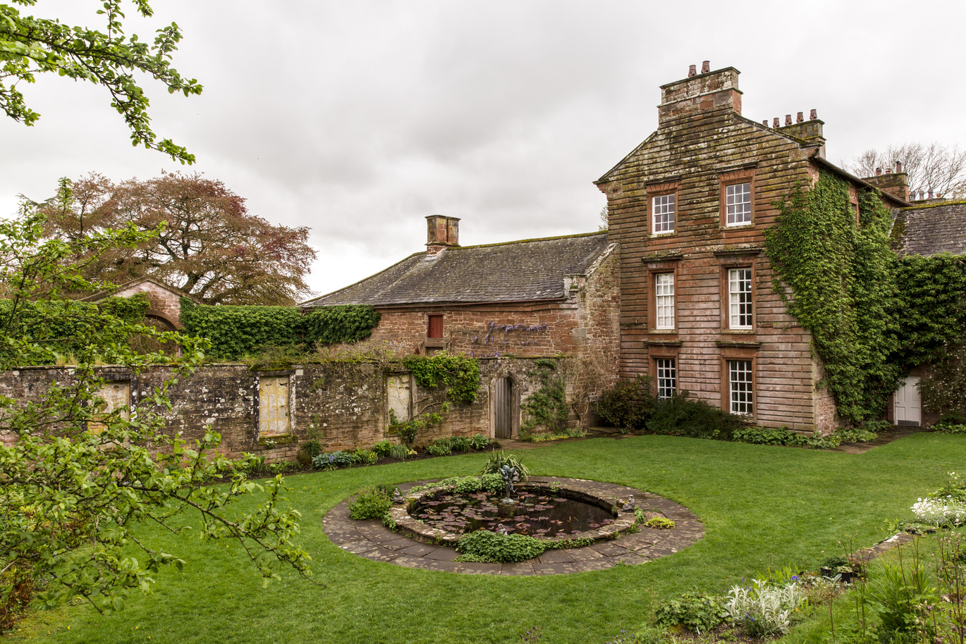 The Lily pond in the middle of the lawn with the manor house in the background at Acorn Bank.