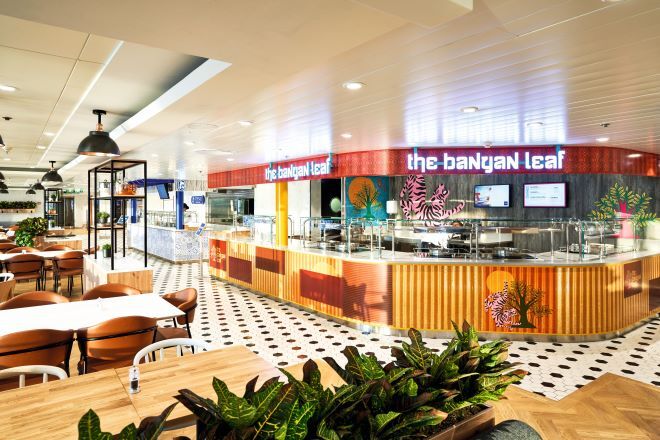 "A restaurant called 'The Banyan Leaf'. There is a large counter and tables and chairs in the restaurant with a planter in the foreground with foliage in. The restaurant has an Asian theme including artwork of tigers and trees."