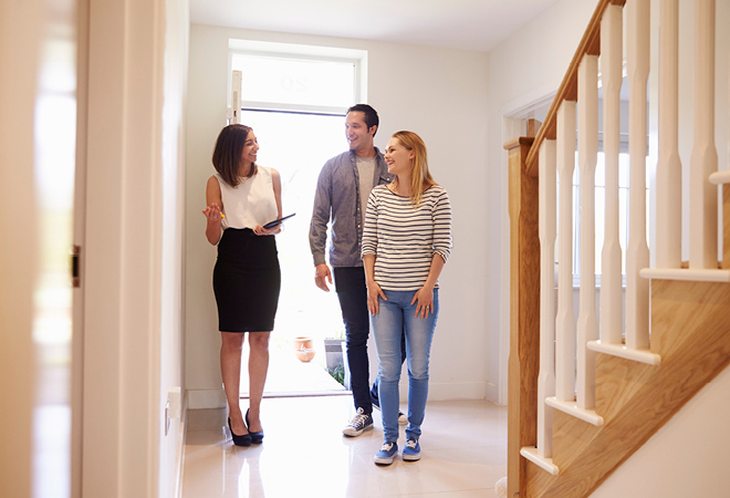 "An estate agent is showing a couple around in a empty house. it's very bright, and everyone is smiling"