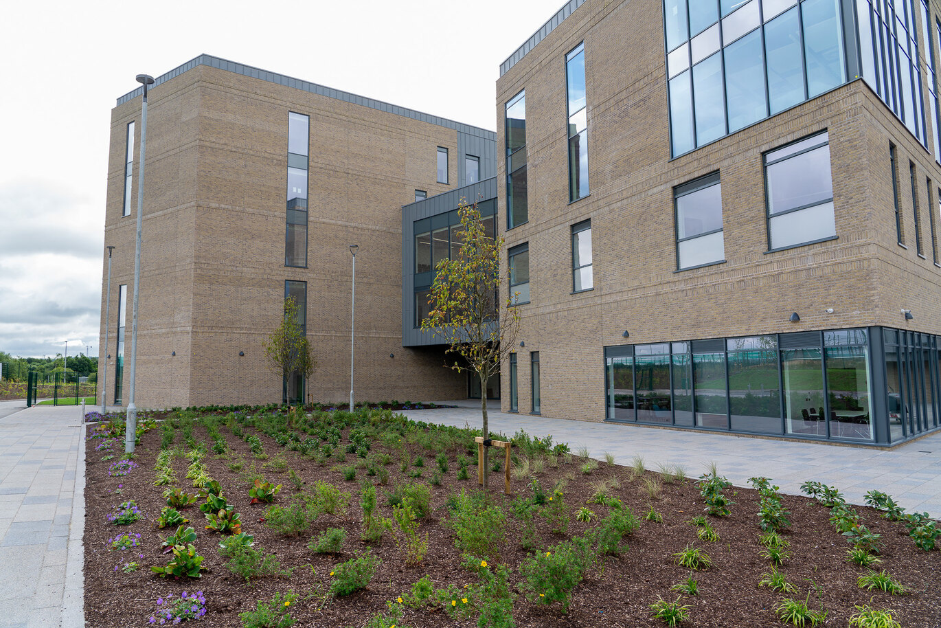 The exterior of a campus building with brown brick and large modern windows, with freshly planted greenery in front