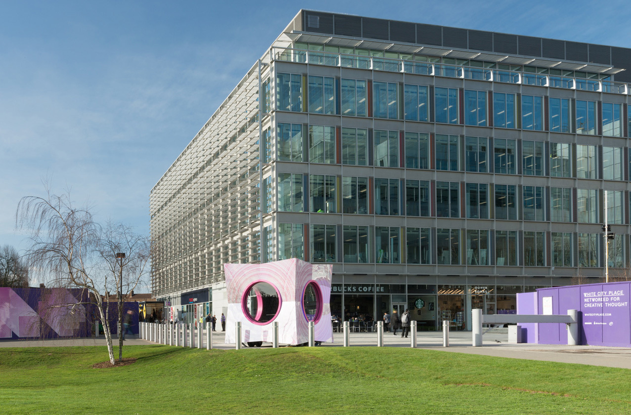 "Large grey building in fron of a green with white bollards"