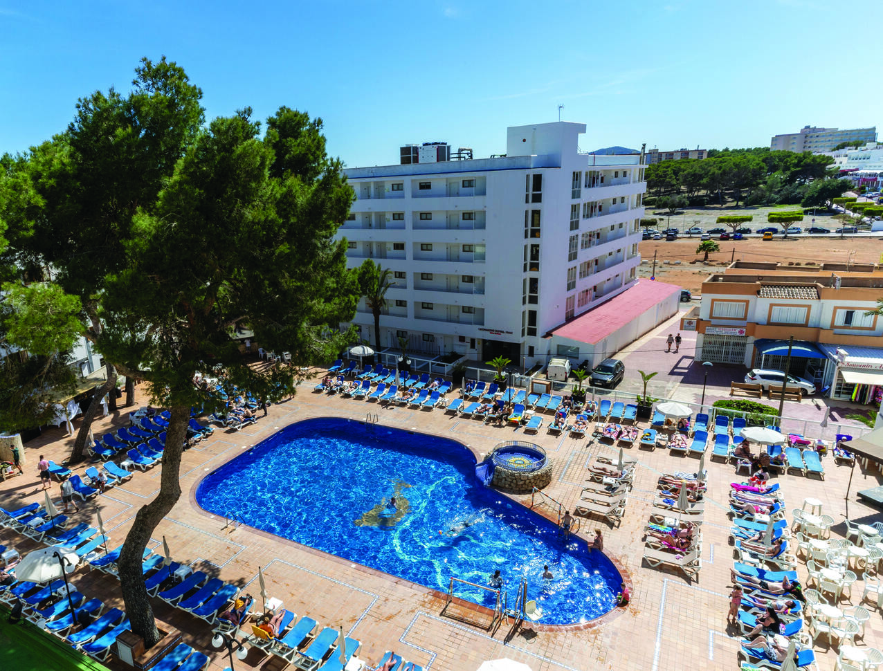 Aerial view of the pool area surrounded by people sunbathing on sun loungers with the hotel building behind.