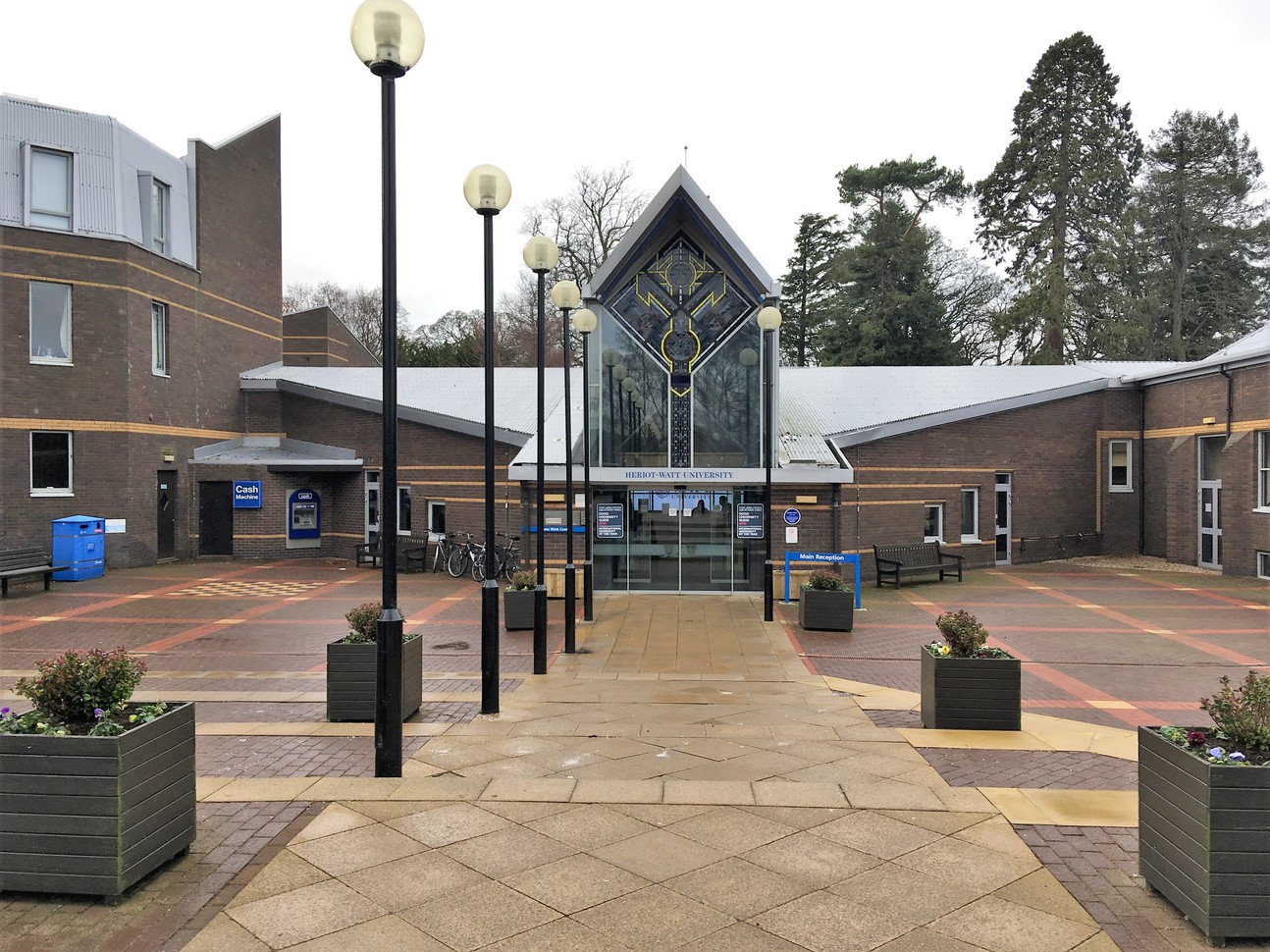 "University building entrance with pedestrianised area leading to door lined with globe lamps"