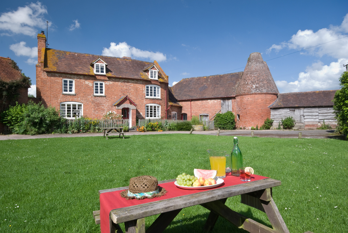 The exterior of Hop Kiln Farmhouse with a picnic bench set up on the large lawn in front.