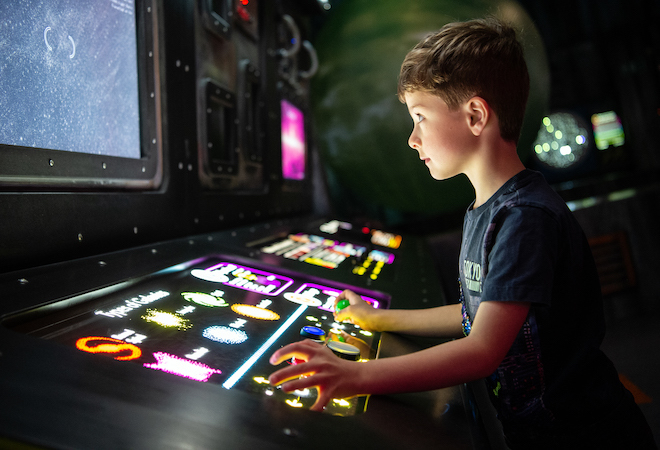 "Photo of a young boy playing a video game machine."