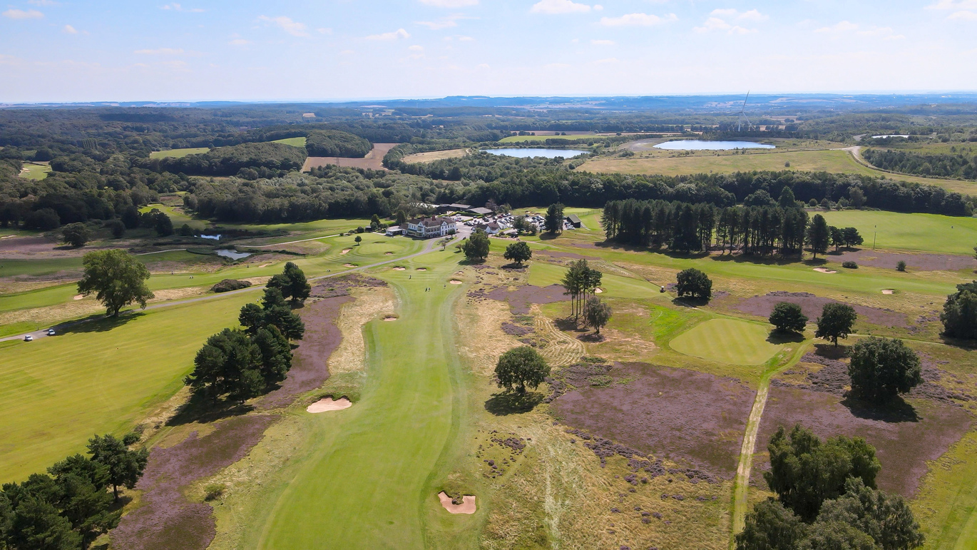 Aerial view of the golf course with the building and car park behind.