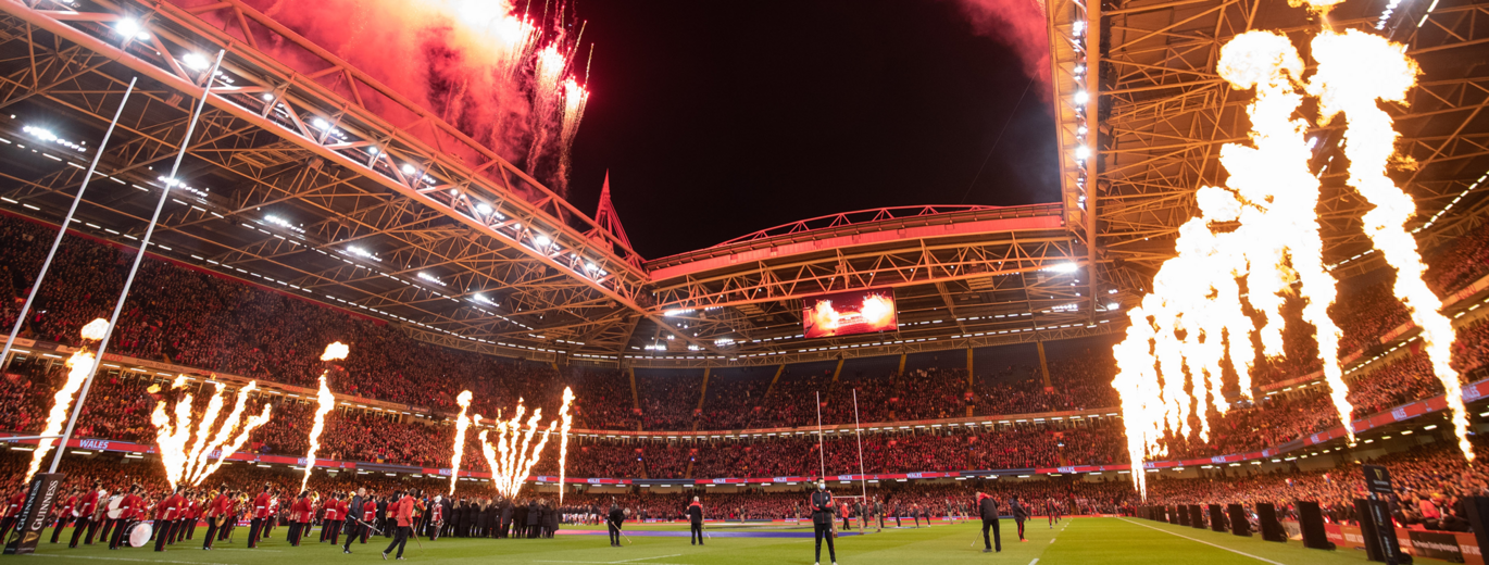 "Rugby Stadium lit up with fireworks and red lights showing the stands and part of the pitch"
