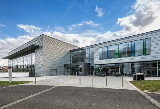 "Exterior image of large modern building with blue sky in background and car park in front"