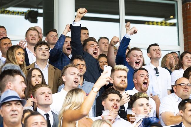 "A group of people cheering on their horses in the crowd"