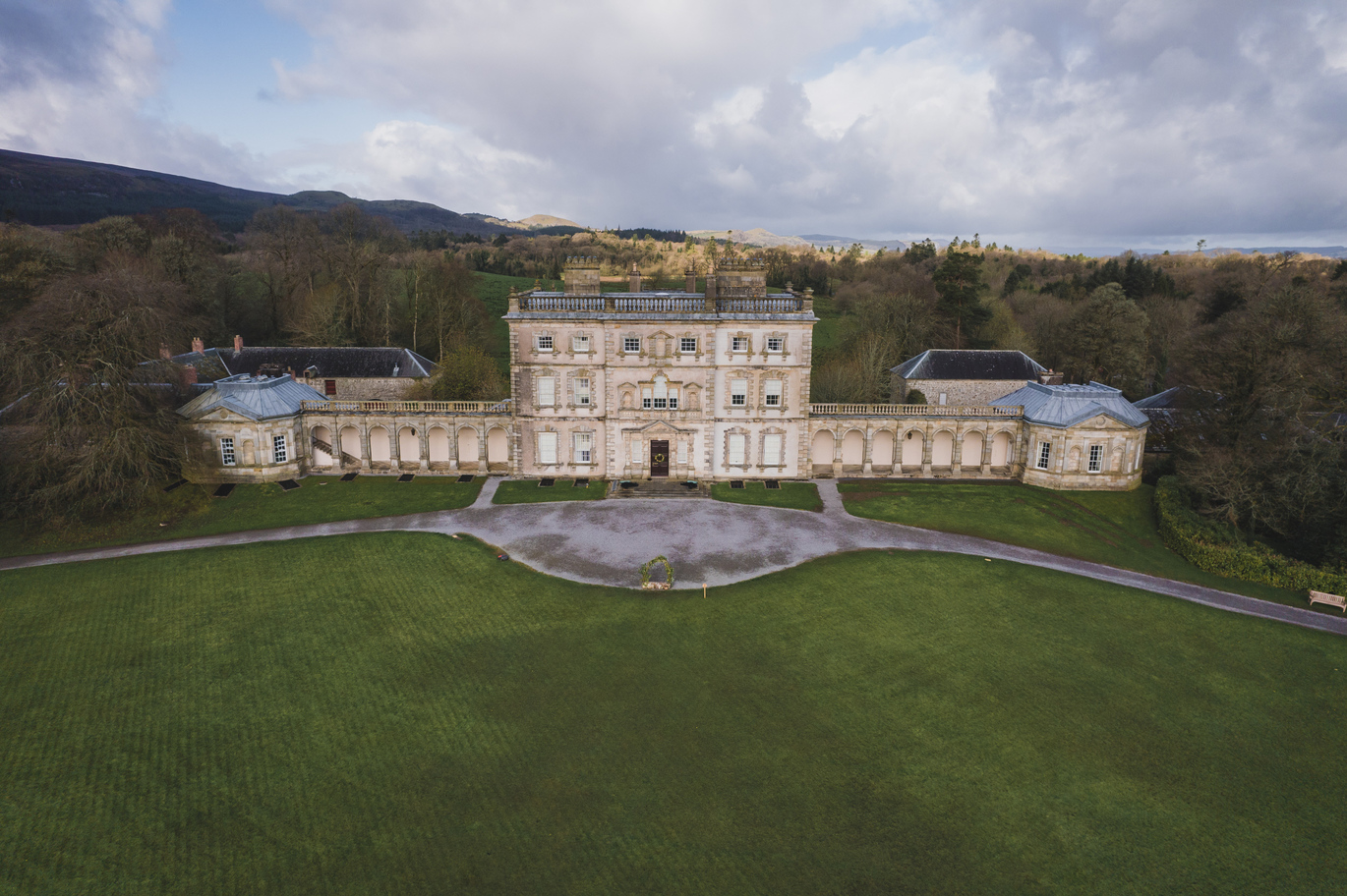 Aerial view of the entrance front and colonnades of Florence Court, with lush green lawns out the front and many trees behind.