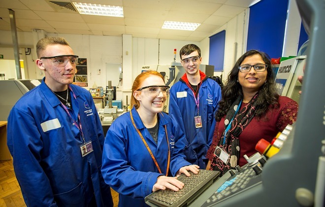 "Photo of 4 people around a machine looking at the screen and wearing safety goggles"